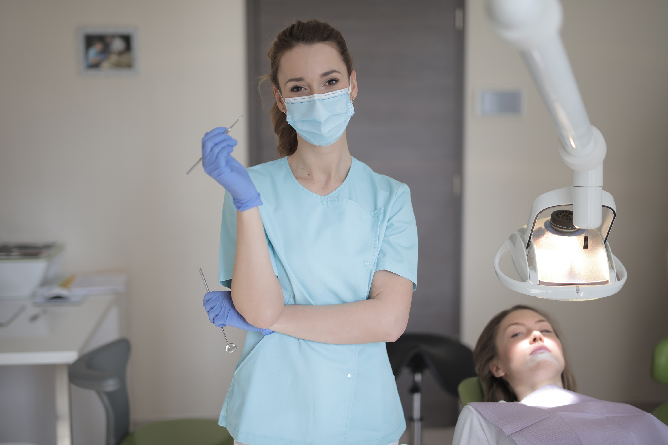 Young female dentist in medical mask and gloves standing in room and looking at camera